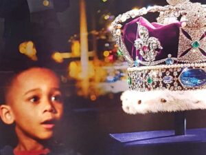 Cropped photo of a billboard at St Pancras in 2019 showing a black boy gazing longingly at the crown jewels