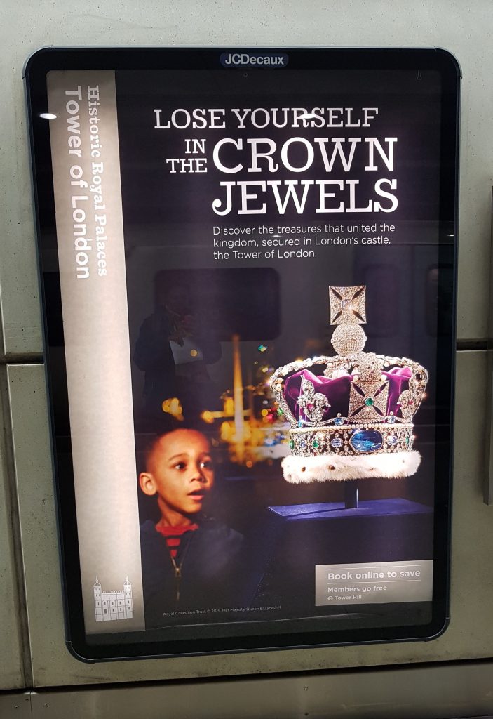 Billboard on St Pancras platform in 2019 advertising the Tower of London with an image of a young black boy gazing with longing at awe at the crown jewels