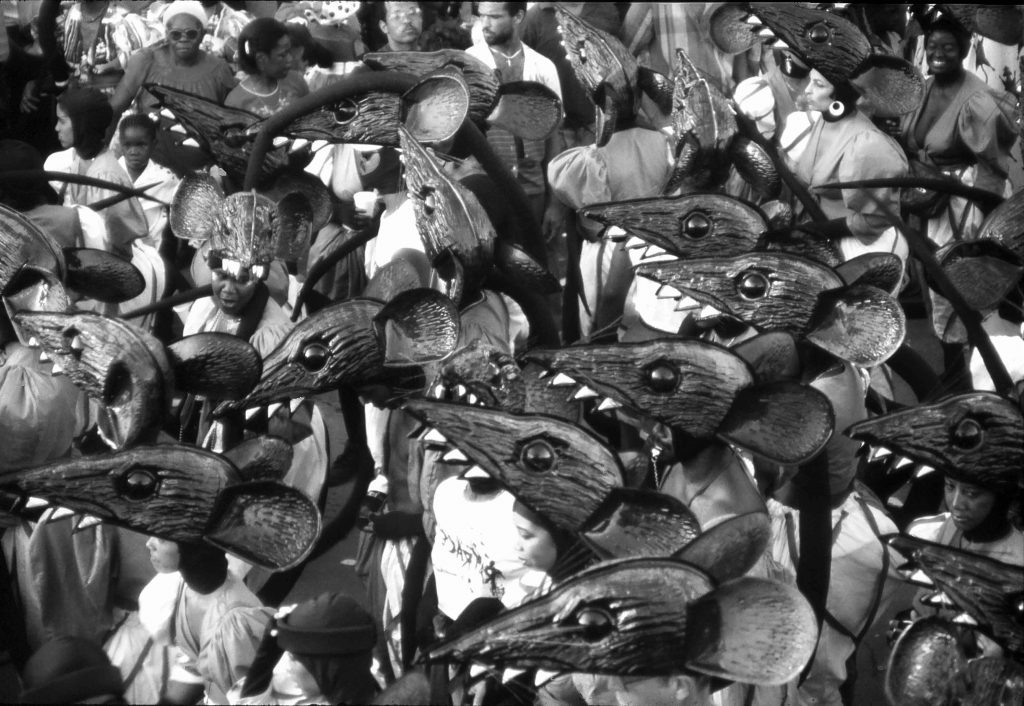 Photo of people in carnival costumes with plastic moulded rat heads for head pieces. All together they look like a horde of rats dancing down the street