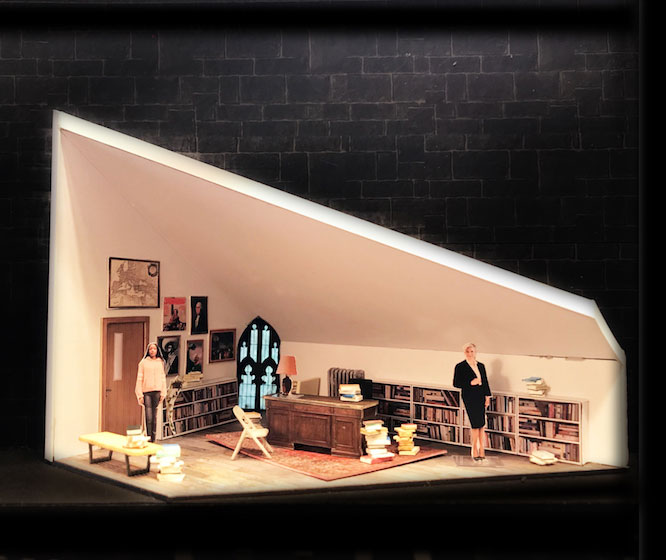 Angled set design showing a sloping ceiling in a room with 2 people