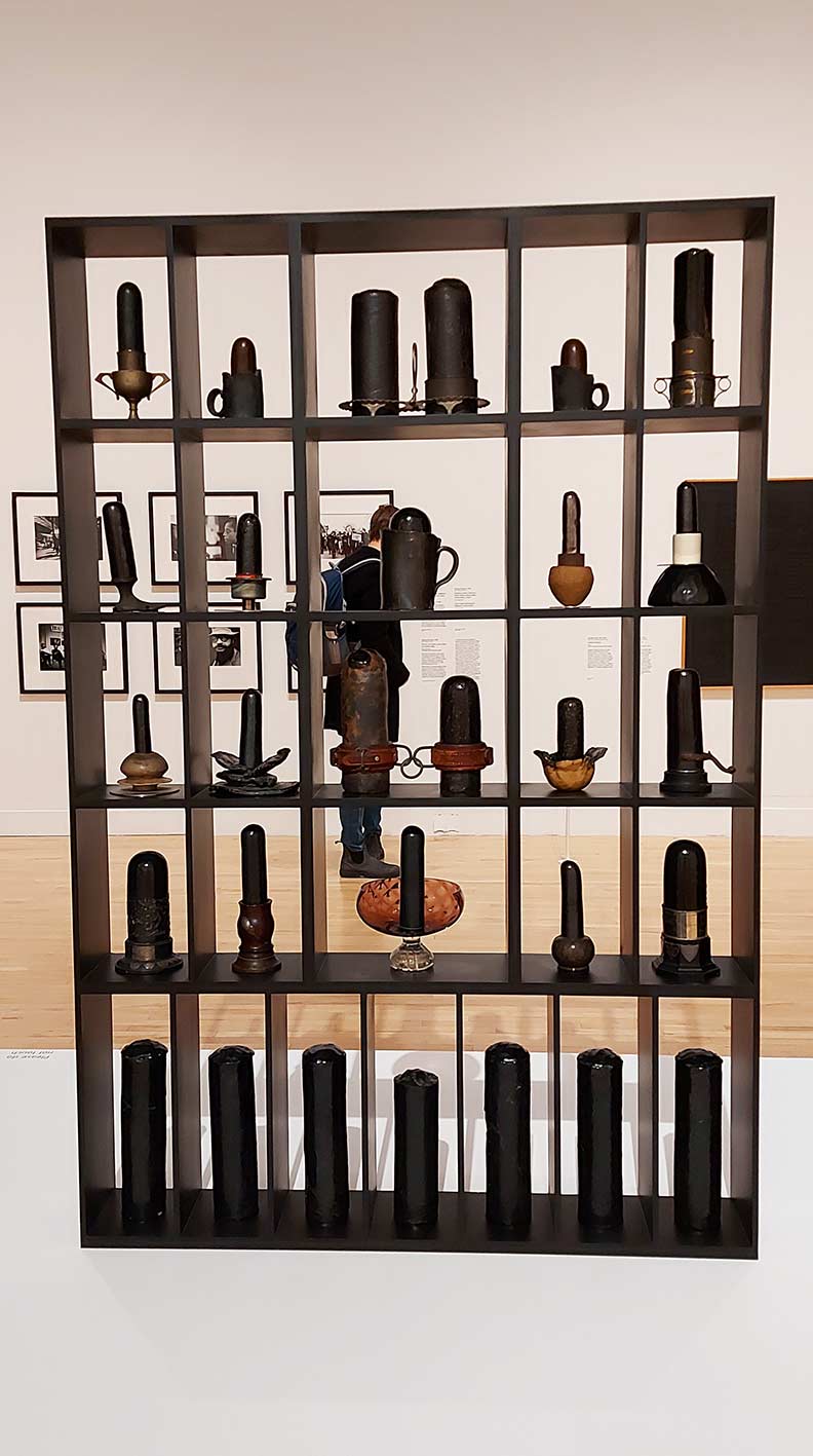 a tall dark wooden curio case of bullet or phallic shaped items on display