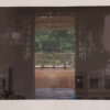 a sepia-toned image of a Caribbean colonial front room with the double doors open. Through the doors is view of highly polished wooden veranda with a view of a lush rainforest