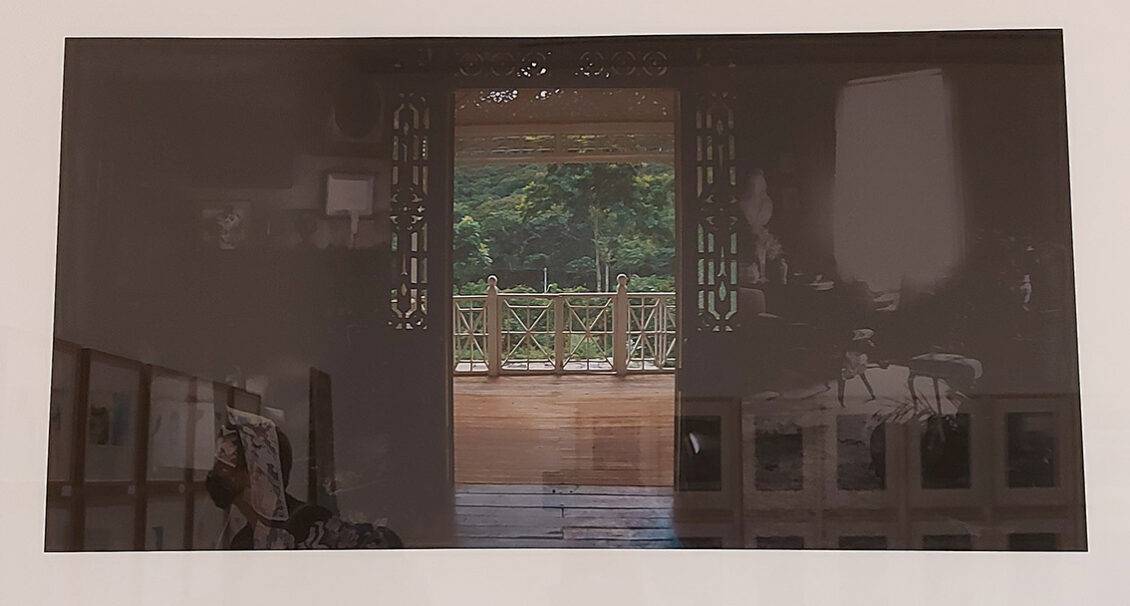 a sepia-toned image of a Caribbean colonial front room with the double doors open. Through the doors is view of highly polished wooden veranda with a view of a lush rainforest