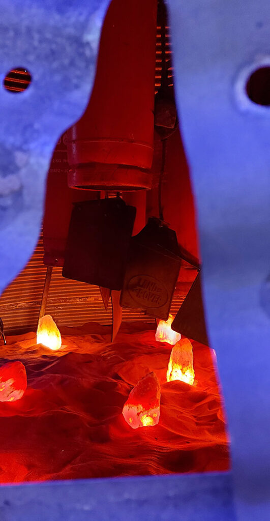 close up of the 'heat source' inside the kiln showing base of the dangling gas canisters and rubber paddles wafting the heat to the incandescent rocks amidst thick sandy base of the kiln