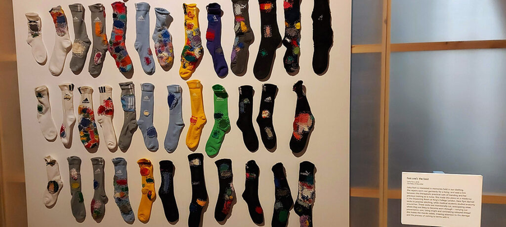 A large white wall with many colourfully darned socks pinned to it