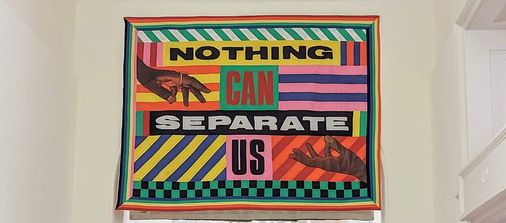 colourful patchwork quilt banner with geometric shapes and lines showing 2 Black hands reaching for each other with the words Nothing Can Separate Us boldly in the middle