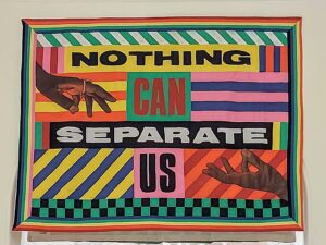 colourful patchwork quilt banner with geometric shapes and lines showing 2 Black hands reaching for each other with the words Nothing Can Separate Us boldly in the middle