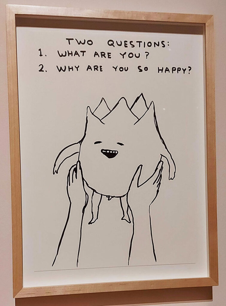 a wood framed line drawing, black ink on cream paper depicting to hands holding up a pudgy life form with a blob-like body and tiny legs and arms. It's smiling with the textnext to it reading: Two Questions. 1. What are you? 2. Why are you so happy?