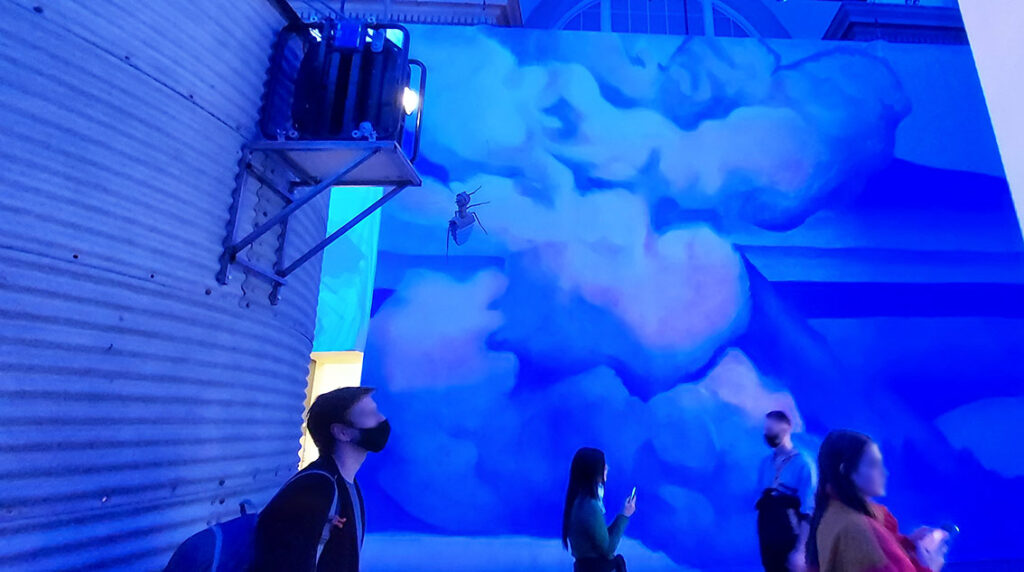 People watching a projection (not in shot) with cloud-painted backdrop
